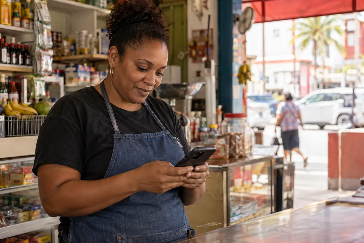 Trinidad shop owner checking her new mobile app on her phone at the counter